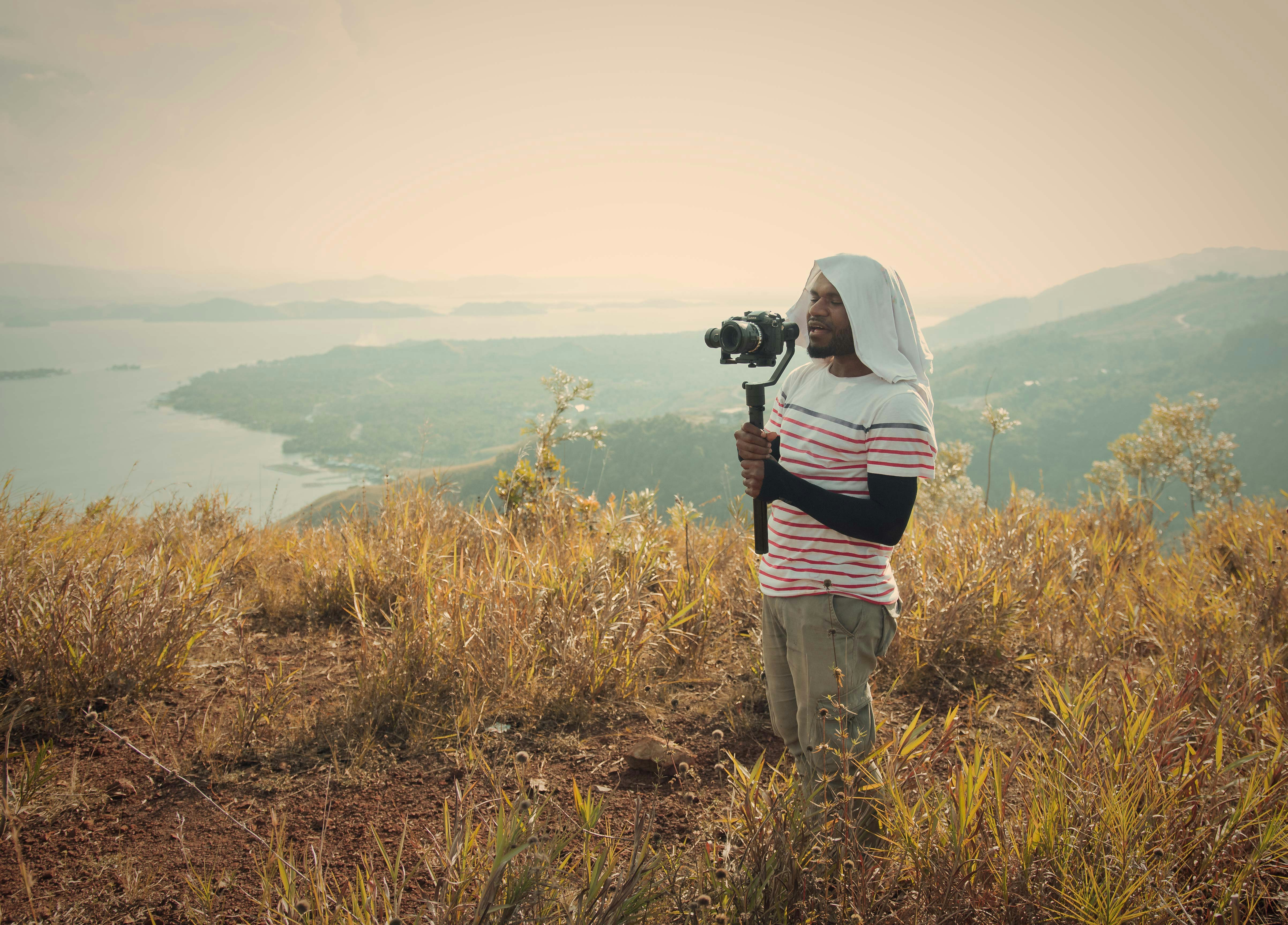 woman in white and black stripe hoodie holding black dslr camera standing on green grass field